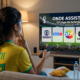 Torcedora brasileira no sofá diante da tela da TV em dúvida sobre onde assistir o jogo do Brasil na Cpa do Mundo 2026