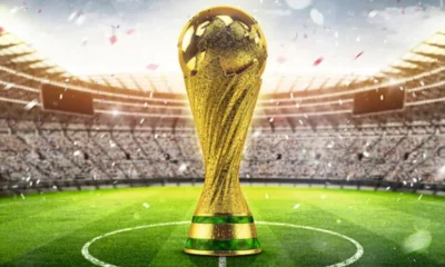 Imagem da Taça FIFA no centro de um gramado de um estádio de futebol lotado